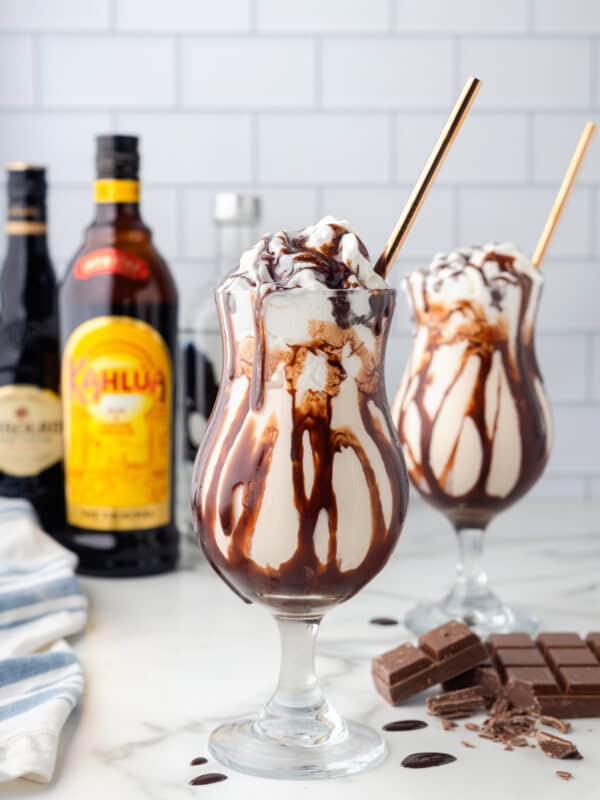 2 frozen mudslides with gold straws in front of bottles of alcohol.