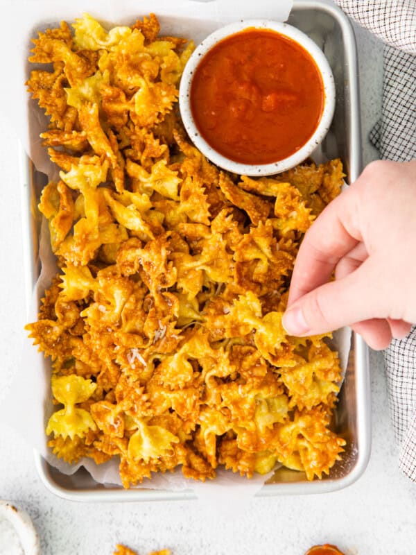 a hand grabbing a garlic parmesan pasta chip from a platter with marinara sauce.