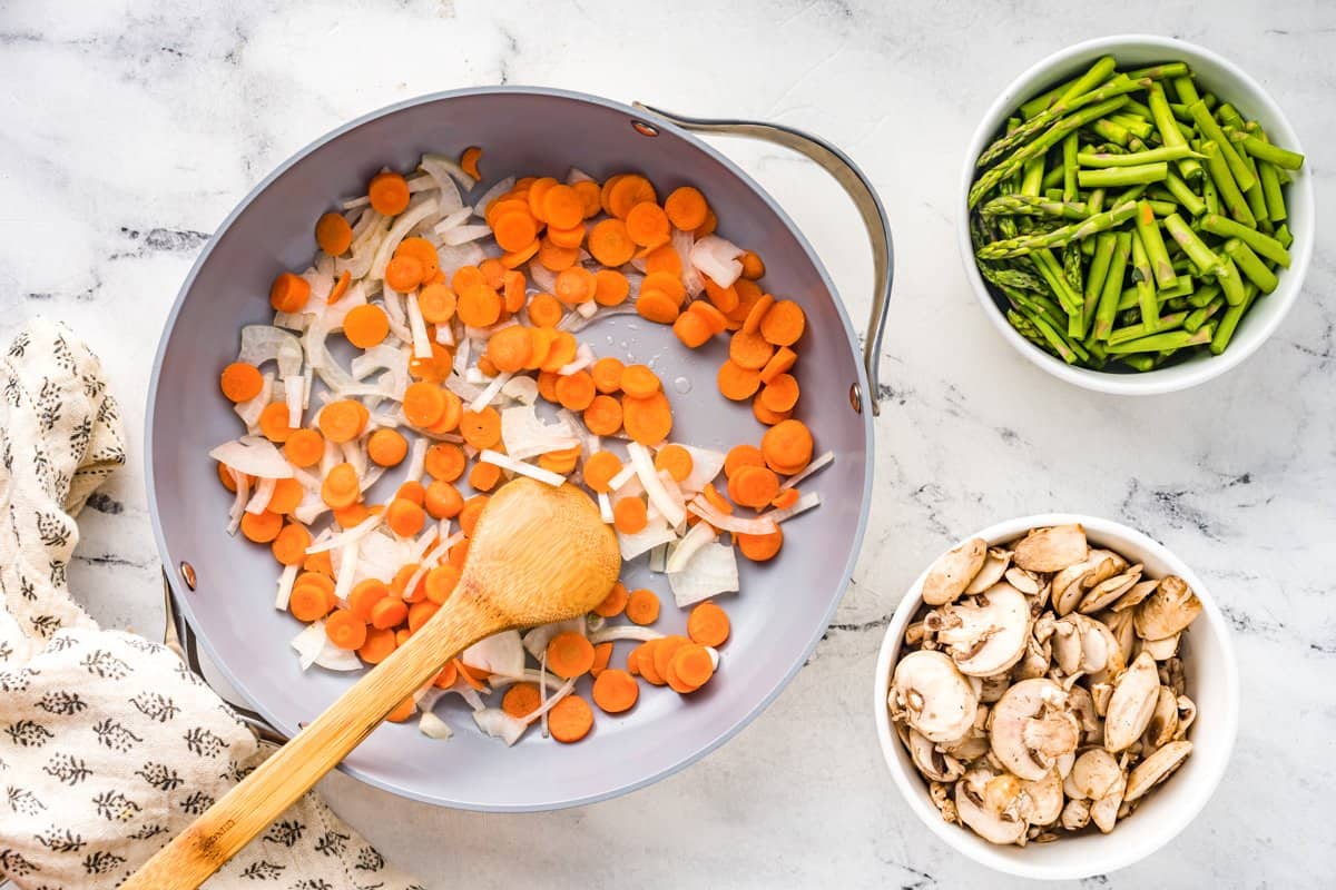 sautéing carrots and onions in a pan with a wood spoon.