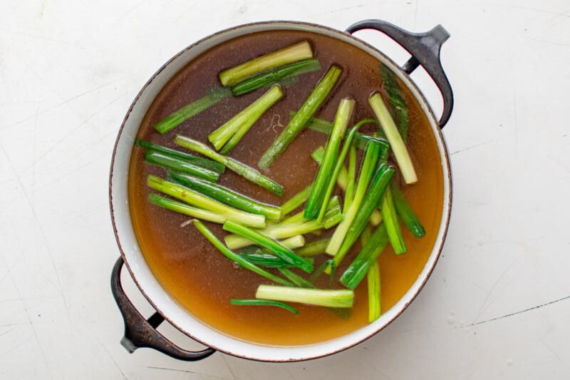 egg drop soup broth with green onions in a black pot.