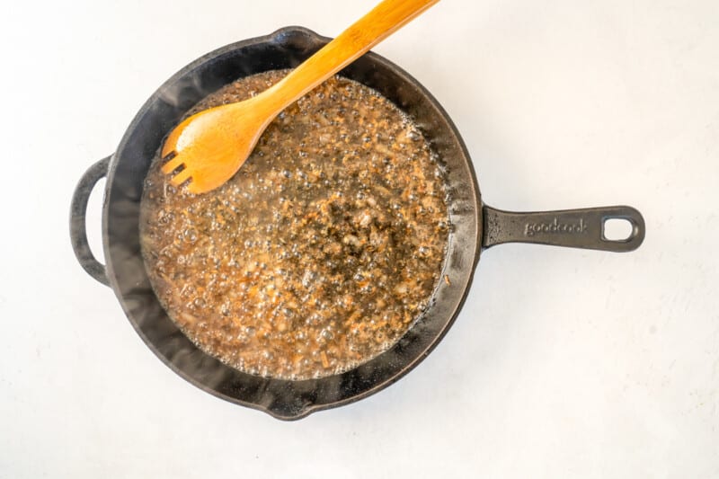 Overhead view of a skillet being deglazed with a wooden spoon.