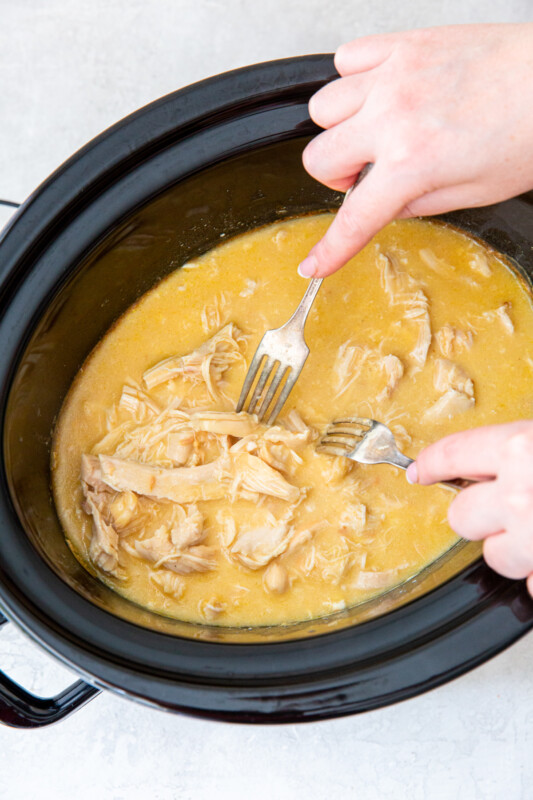 2 forks shredding chicken and gravy in a crockpot.