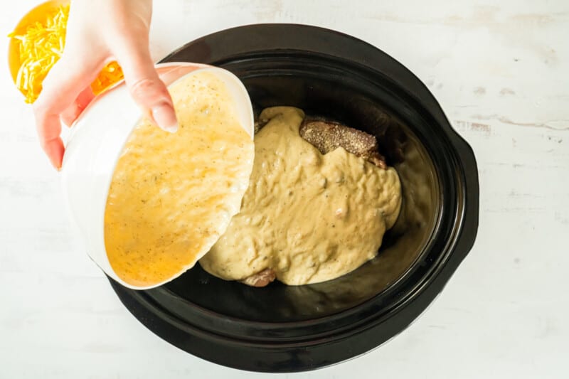 soup mixture poured over chicken and rice in a crockpot.