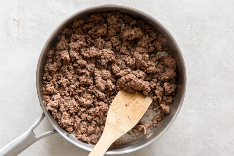 cooked ground beef in a skillet with a wood spoon