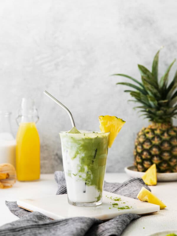 pineapple matcha drink on a white trivet with a stainless steel straw..