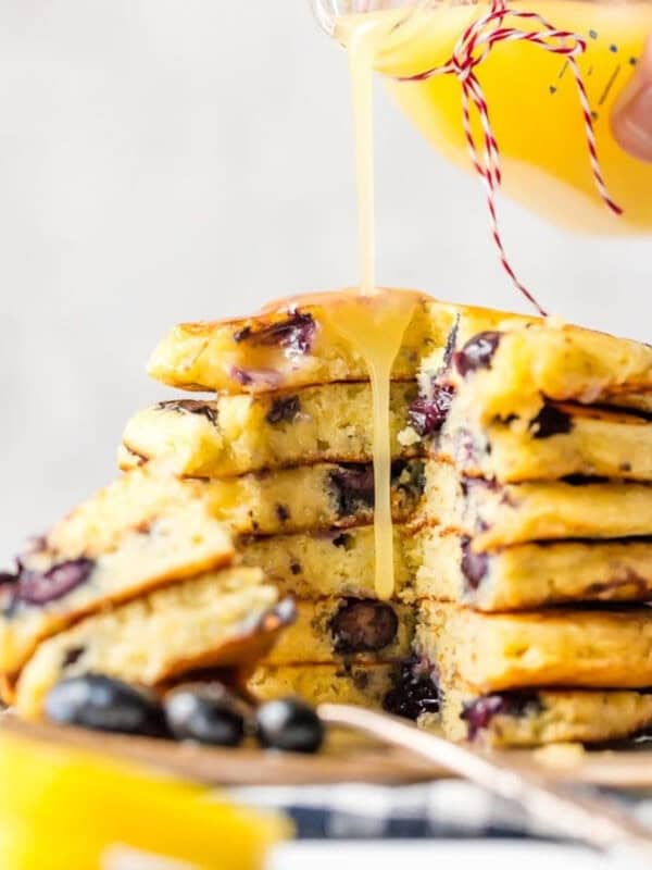 A stack of blueberry pancakes being drizzled with lemon juice and chocolate sauce.