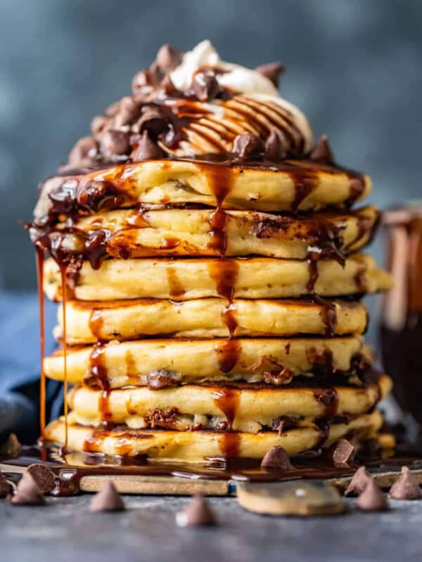 A stack of chocolate pancakes with chocolate syrup and chocolate chips.