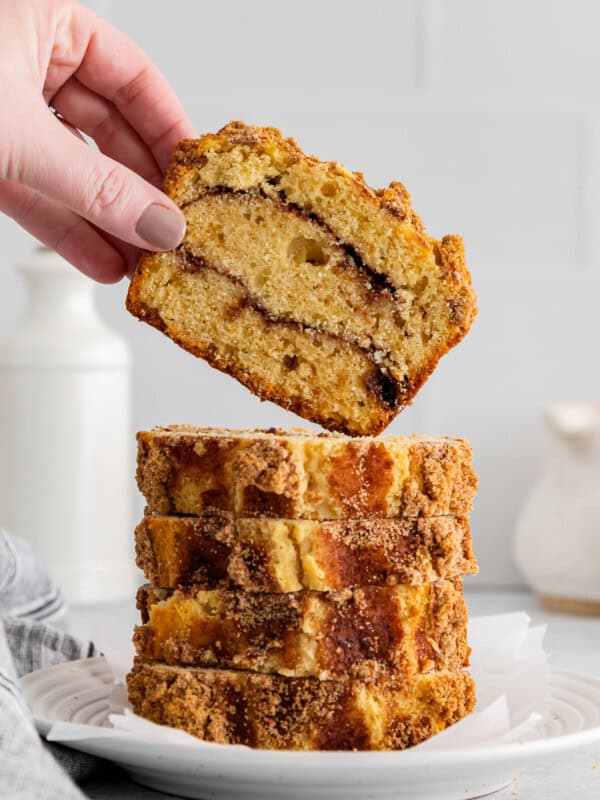 hand grabbing 1 of 5 slices of cinnamon roll bread stacked on a white plate.