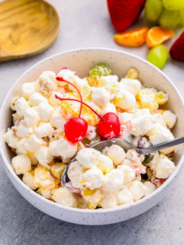 marshmallow salad in a white bowl with 2 maraschino cherries and a spoon.