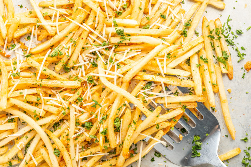 garlic parmesan fries on a sheet pan with a spatula.