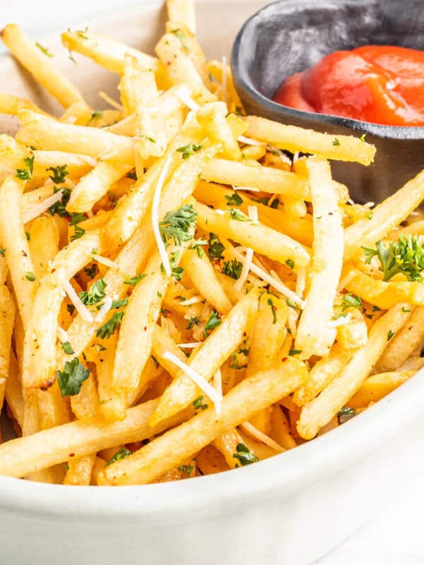 garlic parmesan fries in a white bowl with ketchup.