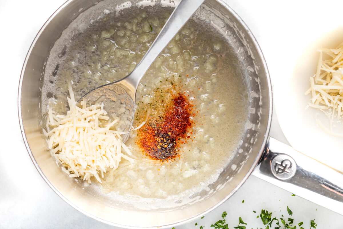 cayenne and parmesan added to garlic butter in a saucepan with a spoon.