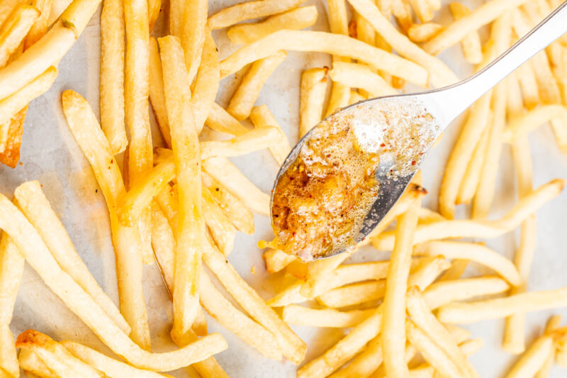 garlic parmesan butter spooned over baked french fries on a sheet pan.