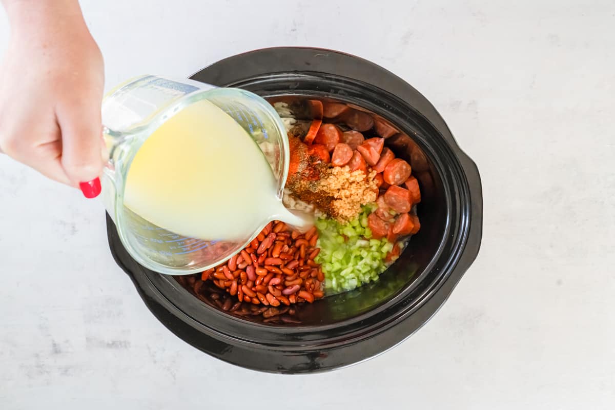 chicken broth poured over ingredients for red beans and rice in a crockpot.