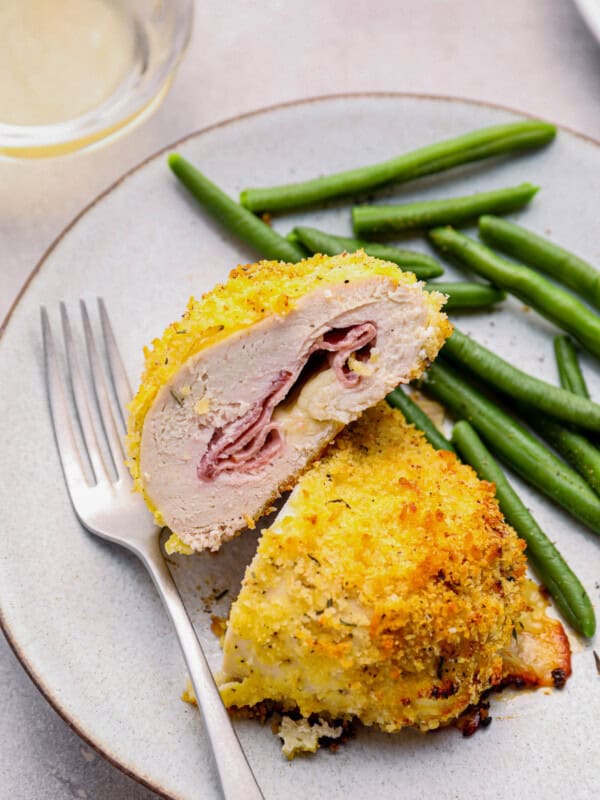 sliced chicken cordon bleu baked on a white plate with green beans and a fork.