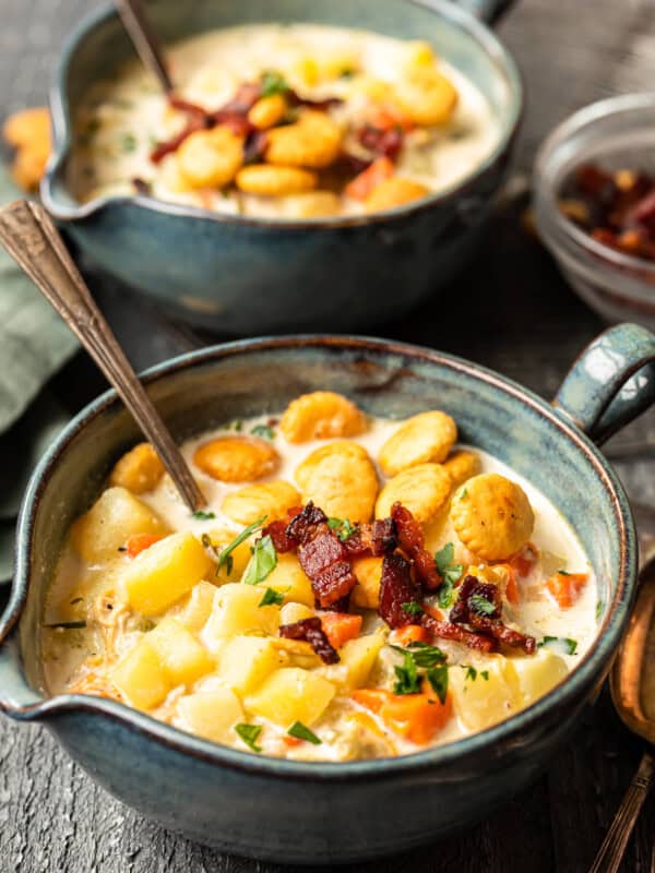 new england clam chowder in gray bowls with oyster crackers and spoons.