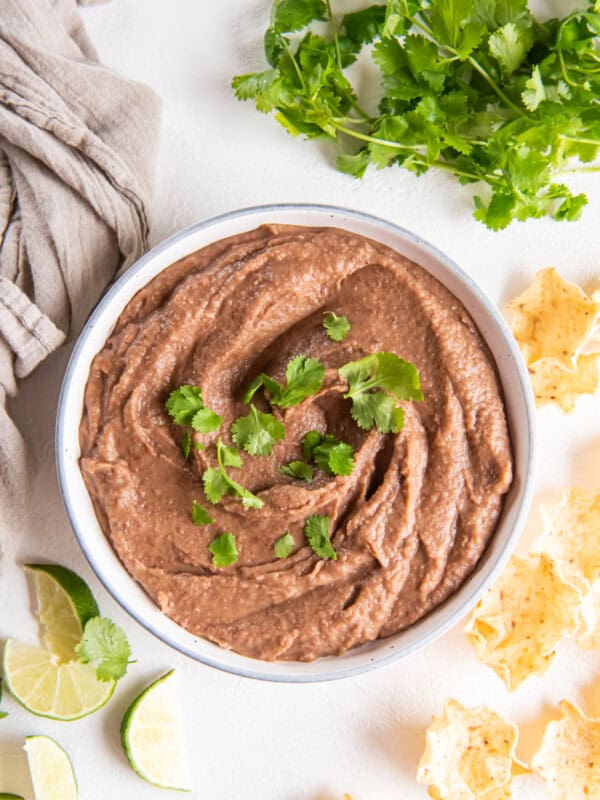 crockpot refried beans in a white bowl with cilantro.