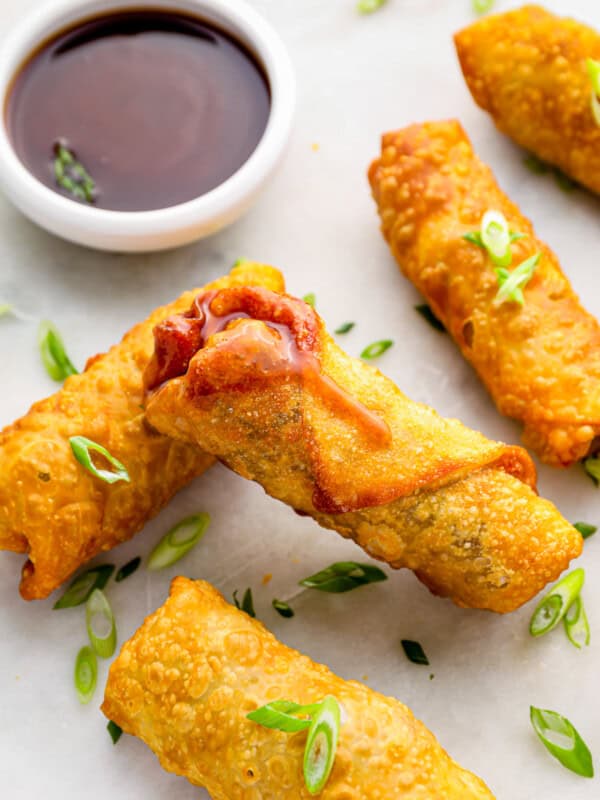 5 egg rolls on a white plate with dipping sauce.