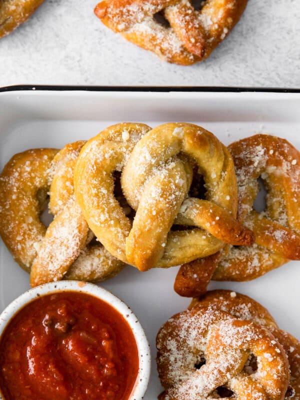 close up of garlic parmesan soft pretzels in a white serving tray with marinara sauce.