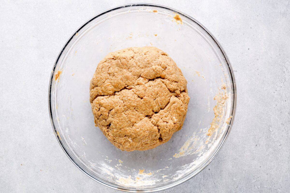 A ball of peanut butter dog treat dough in a glass mixing bowl, slightly rough in texture, ready to be rolled out.