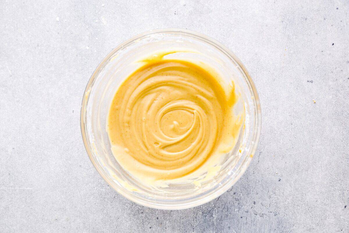 A bowl of smooth, golden peanut butter frosting with a creamy consistency, ready for decorating dog treats.