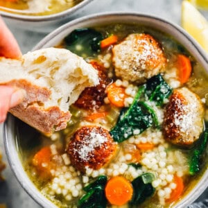 dipping a piece of bread into italian wedding soup