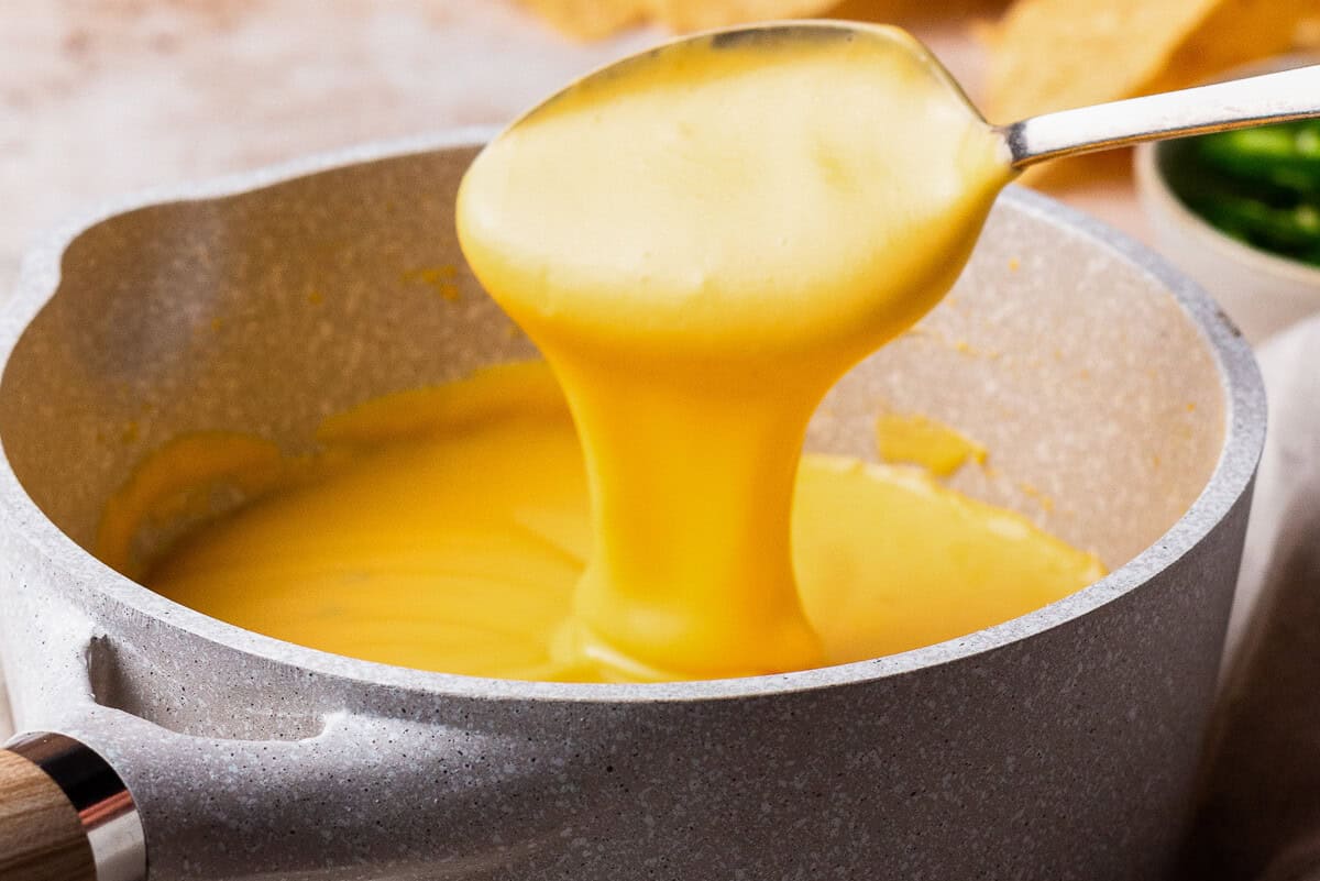 spoon dipping into a pot of cheese sauce