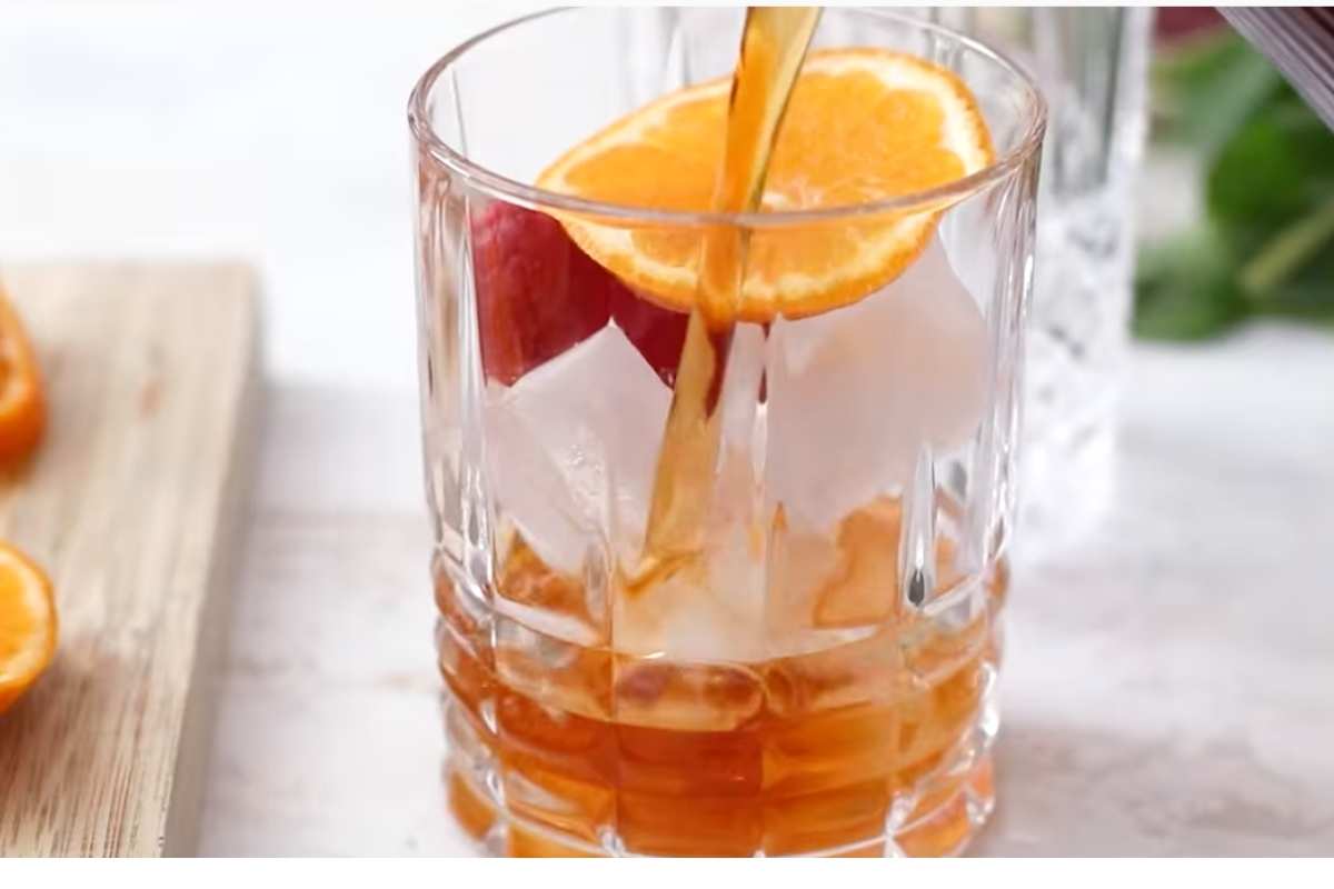 Pouring spiked raspberry sweet tea in a glass filled with ice cubes.