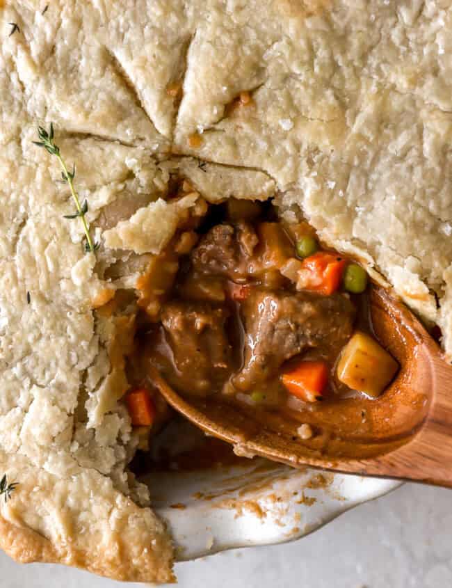 closeup overhead view of a cut beef pot pie with the filling exposed on a wooden spoon.