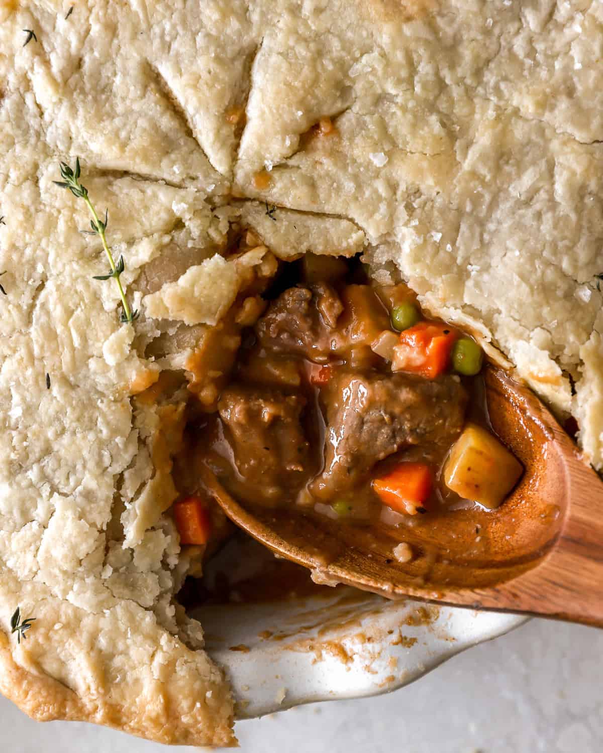 closeup overhead view of a cut beef pot pie with the filling exposed on a wooden spoon.