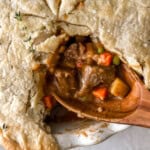 closeup overhead view of a cut beef pot pie with the filling exposed on a wooden spoon.