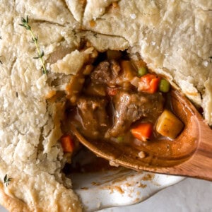 closeup overhead view of a cut beef pot pie with the filling exposed on a wooden spoon.