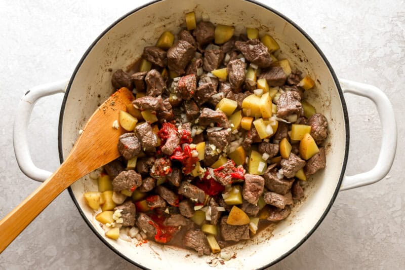 seasoned cubed beef, potatoes, and onions in a pan with a wooden spoon.