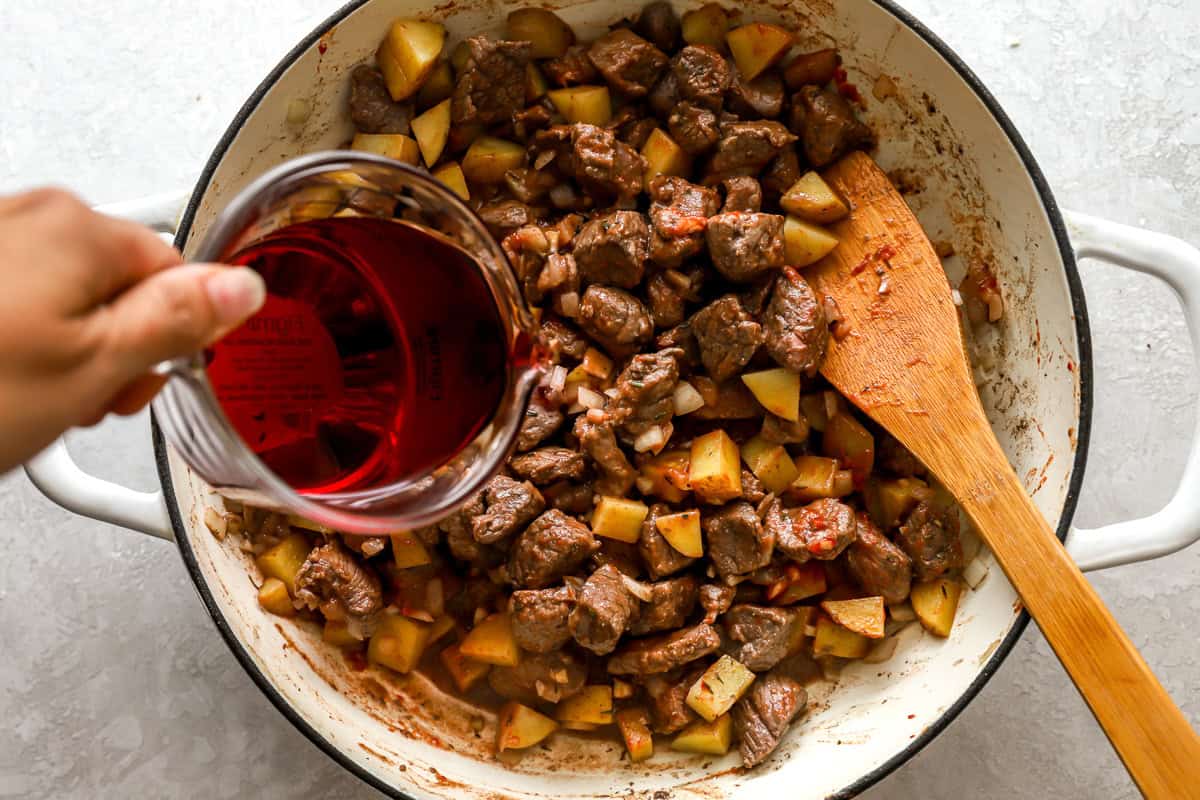 deglazing a pan of seared cubed steak and potatoes with red wine.