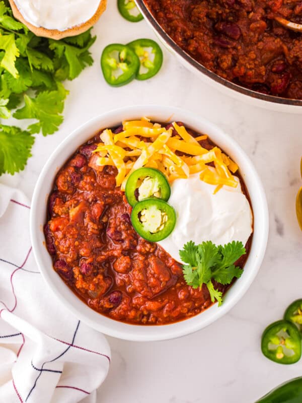 overhead view of chili con carne in a white bowl with cheese, sour cream, jalapenos, and cilantro.