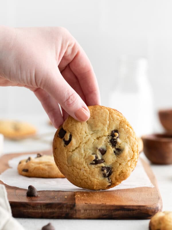 a hand holding a cake mix chocolate chip cookie vertically on a cutting board.