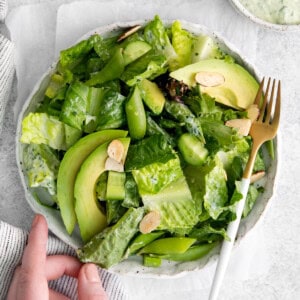 a hand reaching towards a bowl of green salad