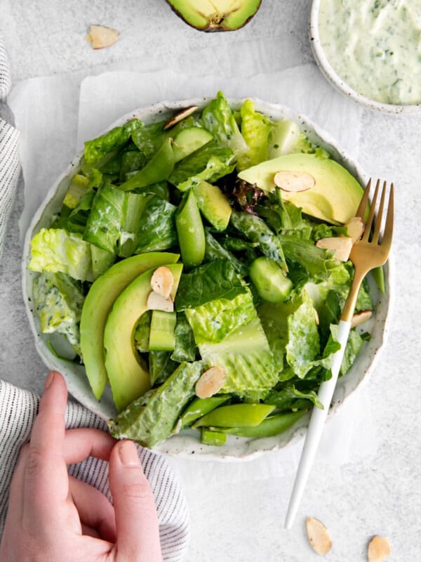 a hand reaching towards a bowl of green salad