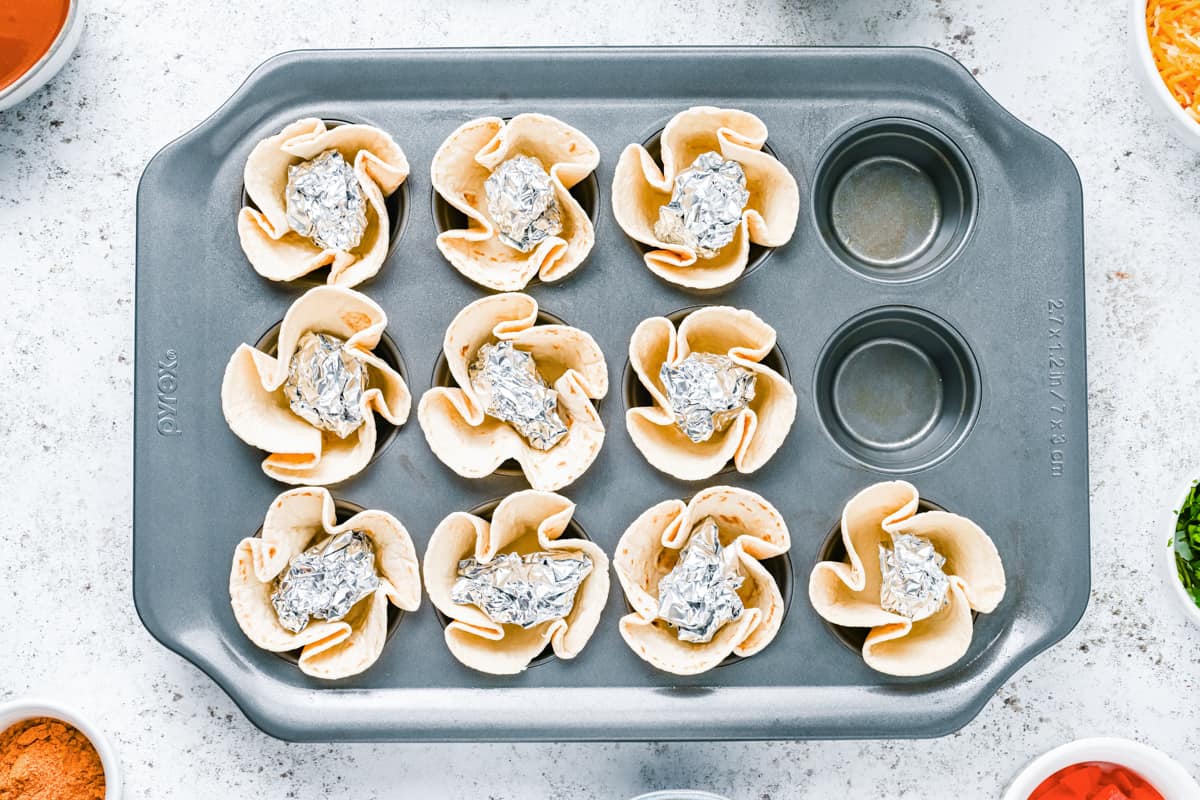 flour tortillas formed into cups in a muffin tin with aluminum foil inside.