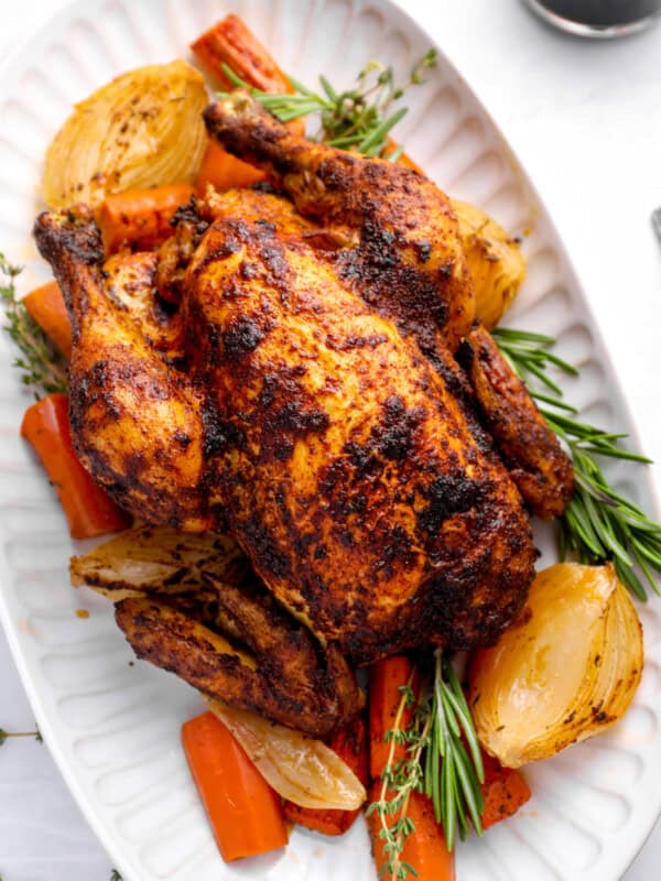 crockpot whole chicken on a white serving platter with vegetables and herbs.