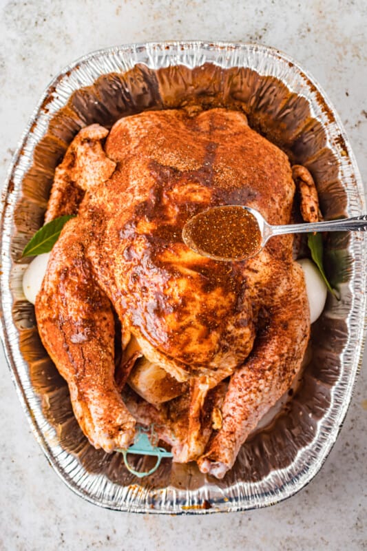 overhead view of juices spooned over a dry brined turkey in an aluminum roasting pan.