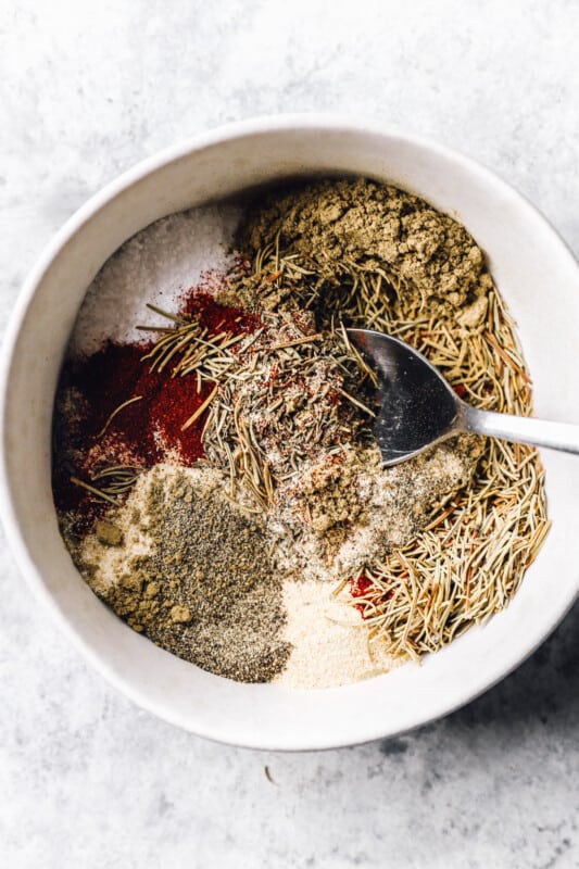 a spoon mixing turkey rub in a white bowl.