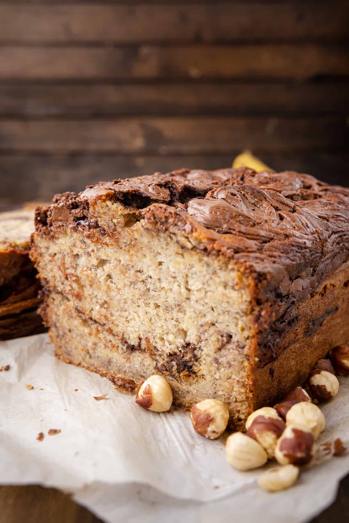 a halved loaf of banana Nutella bread on parchment paper with hazelnuts.