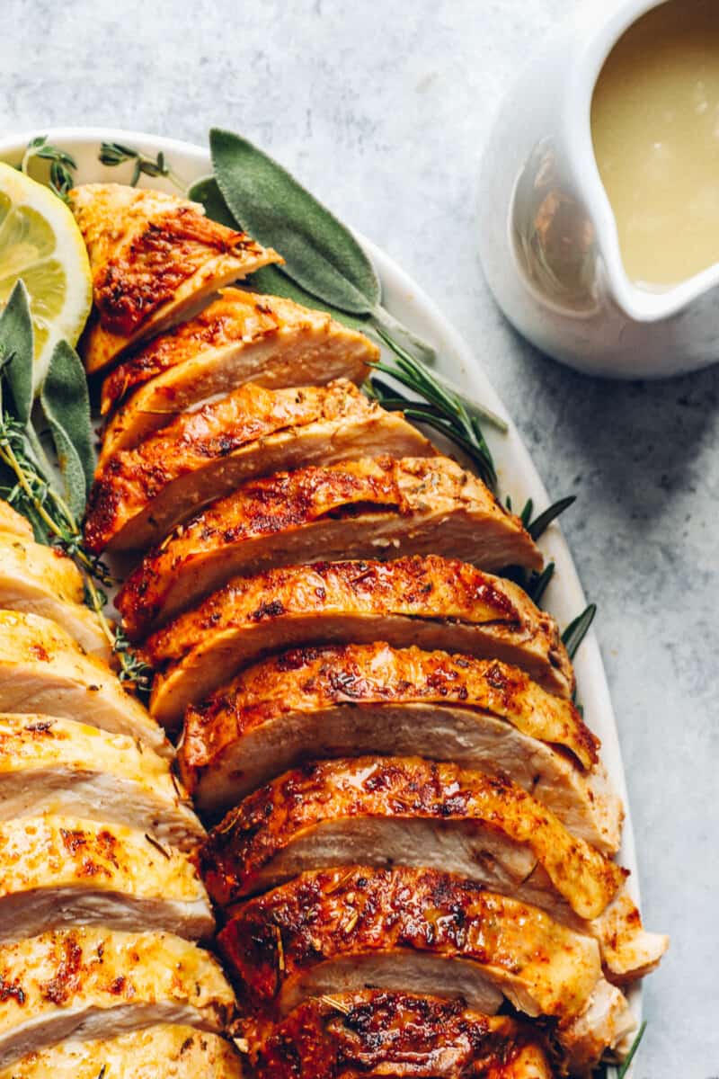 close up of sliced thanksgiving turkey breasts on a white serving platter with lemons and herbs.