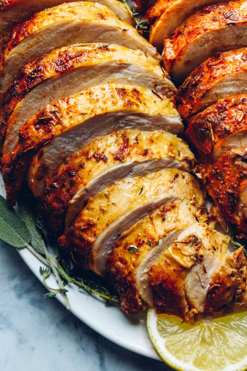 close up of sliced thanksgiving turkey breasts on a white serving platter with lemons and herbs.