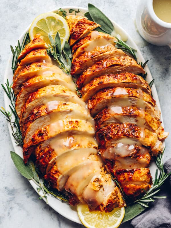 sliced thanksgiving turkey breasts on a white serving platter with lemons and herbs.