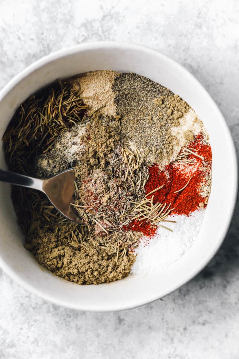 a spoon mixing turkey rub in a white bowl.