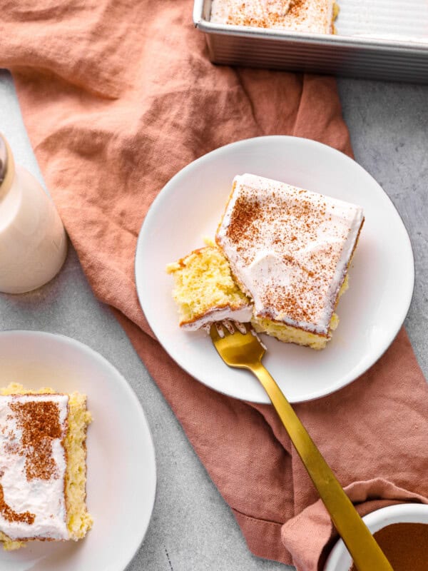 a forkful of tres leches cake resting on a white plate with a slice of tres leches cake.