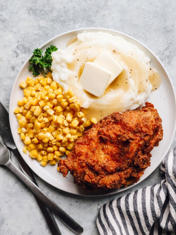 overhead view of a piece of kentucky fried chicken on a white plate with corn and mashed potatoes.