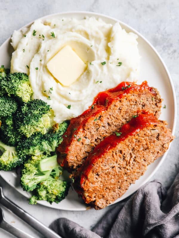 overhead view of 2 slices of crockpot meatloaf on a white plate with broccoli and mashed potaotes.